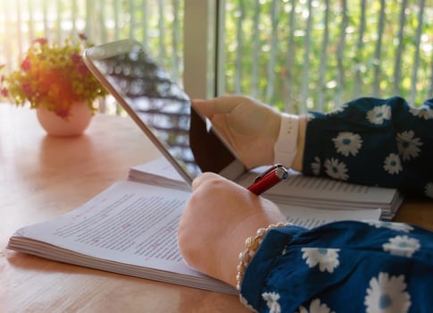 hand holding red pen over blurred paperwork for proofreading photo