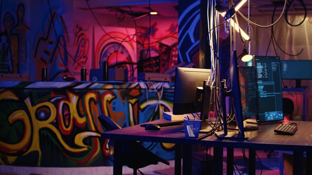 Dolly in shot on computer screen showing programming code and empty pizza boxes in empty warehouse with graffiti sprayed on walls. Hacking software running on PC monitors in underground base photo