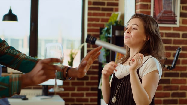 Joyful friends dancing at house party while drinking wine glasses, enjoying celebration. Multiracial group of people having fun indoors, doing entertaining dance moves to music in modern apartment photo