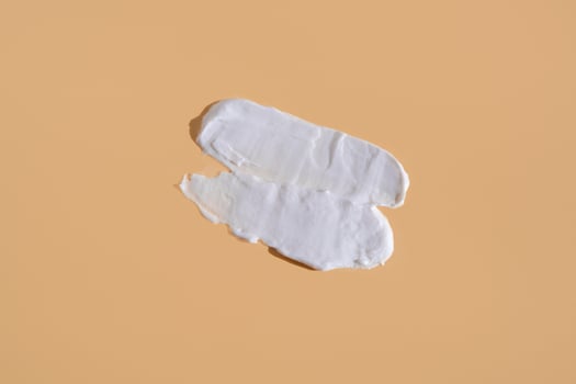 White smear of cosmetic cream on a beige background. Creamy foundation texture isolated. Smear of face cream. Close up of cream texture photo