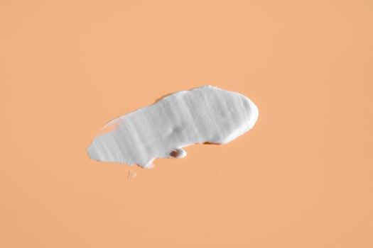 White smear of cosmetic cream on a beige background. Creamy foundation texture isolated. Smear of face cream. Close up of cream texture photo