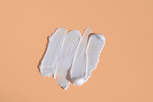 White smear of cosmetic cream on a beige background. Creamy foundation texture isolated. Smear of face cream. Close up of cream texture photo