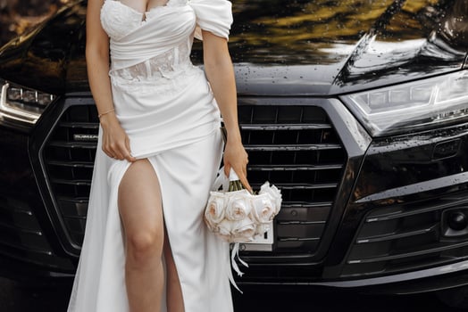 A dark-haired bride stands next to a modern black car on your wedding day with a bouquet of flowers. Portrait of the bride. White dress, long veil photo