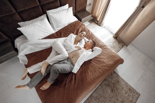Sensual and gentle morning of the bride and groom in the hotel room. Happy and in love bride and groom are lying on the bed. Confident girl-bride and handsome groom. Preparation for the wedding photo