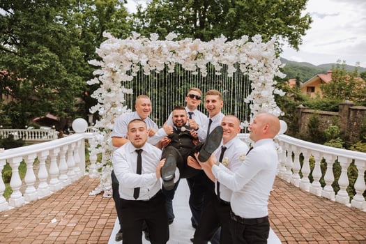 Cheerful, young, energetic witnesses of the bridegroom hold the bridegroom in their arms. Funny photo. The groom in a vest and his friends in white shirts pose near the wedding arch. Wedding in nature photo
