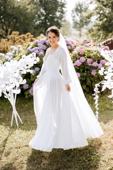 A beautiful brunette bride in an elegant robe is walking in a park with green grass and pink hydrangea flowers. Morning, meetings, wedding portrait of a cute girl. Photography and concept. Summer. photo