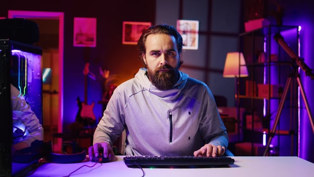 Focused man playing videogames at home, spamming keyboard buttons trying to defeat enemies. Competitive pro gamer trying hard to win online multiplayer esports tournament, zoom out shot photo