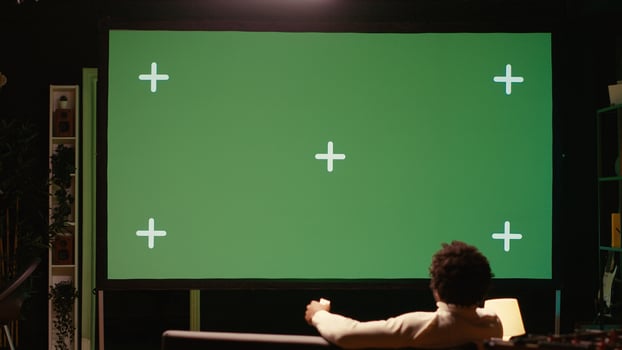 African american man using remote to zap through films available on streaming services on chroma key TV. Cord cutter having movie night in home theatre using green screen television set photo