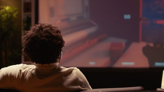 African american man watching video on widescreen smart TV of FPS in dimly lit living room. Player learning to play game by looking at internet guide on television display photo