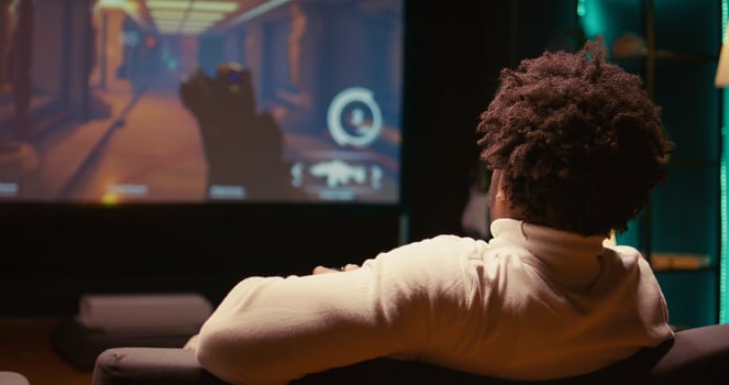 Close up of man plays first person shooter videogame on large smart TV with gun shooting at enemies. Gamer enjoying PvP online multiplayer game with players competing against each other, zoom in shot photo
