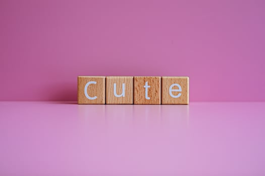 Wooden blocks form the text Cute against a pink background. photo