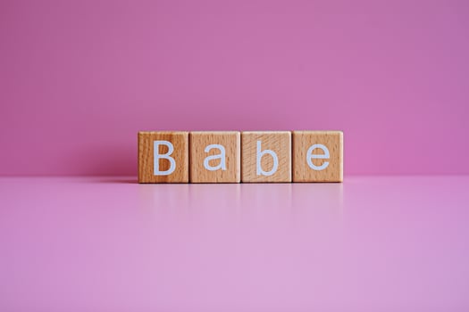 Wooden blocks form the text Babe against a pink background. photo