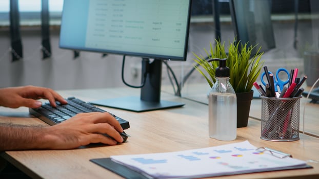 Close up of man using hand sanitizer alcohol gel in office with new normal before working at computer. Entrepreneur sitting in workplace cleaning disinfecting hands against corona virus. photo