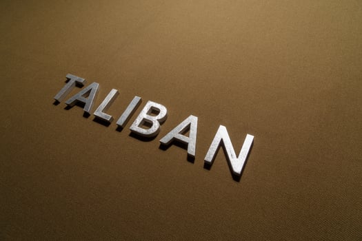 the word taliban laid with silver metal letters on rough tan khaki canvas fabric photo