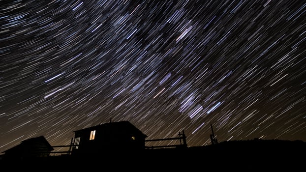 Wooden house in the mountains in winter. Star trails in the night sky. photo