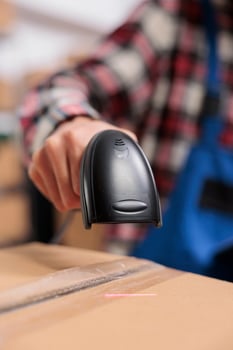 Delivery service employee scanning parcel and managing packages storing in warehouse. Storehouse worker doing shipment operations while holding barcode scanner in hand close up photo