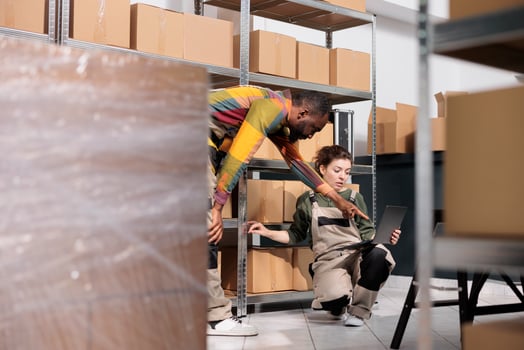 Stockroom colleagues analyzing stock management system on laptop computer and packing customers orders. Shipping company employees preparing cardboard boxes for delivery in warehouse photo