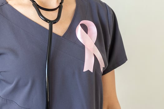 Shot of the female doctor against the white wall with pink ribbon, as a symbol of a breast cancer awareness. Concept photo