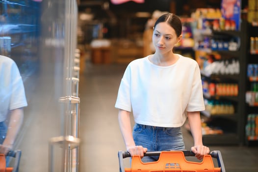 Young smiling happy woman 20s in casual clothes shopping at supermaket store with grocery cart photo