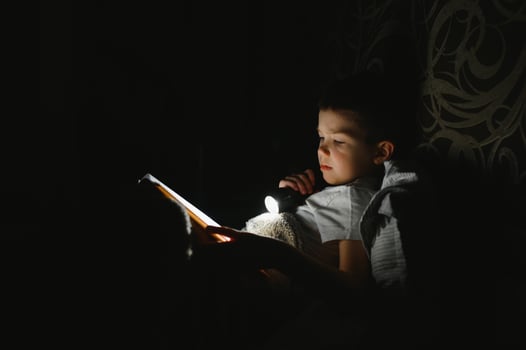 Child reading book in bed. Kids read at night. Little boy with fairy tale books in bedroom . Education for young children. Bedtime story in the evening. Cute kid under blanket in dark room with lamp photo
