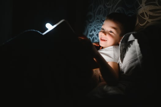 Child reading book in bed. Kids read at night. Little boy with fairy tale books in bedroom . Education for young children. Bedtime story in the evening. Cute kid under blanket in dark room with lamp photo