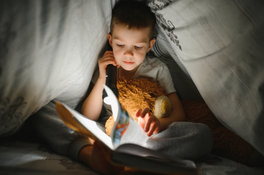Child reading book in bed. Kids read at night. Little boy with fairy tale books in bedroom . Education for young children. Bedtime story in the evening. Cute kid under blanket in dark room with lamp photo