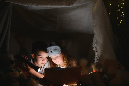Little kids involving in reading amazing book. They lying in nice toy tent in playroom. Boy holding flashlight in hand. photo