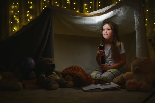 Reading and family games in children's tent. Little girl with books and flashlight before going to bed photo