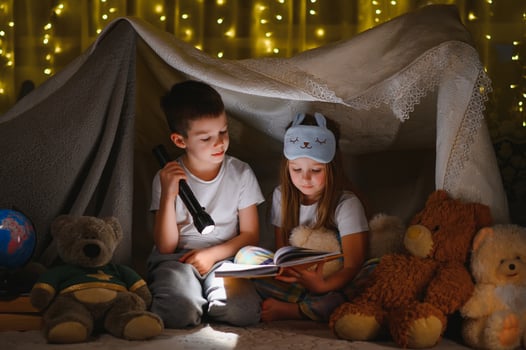 reading and family games in children's tent. boy and girl with book and flashlight before going to bed. photo