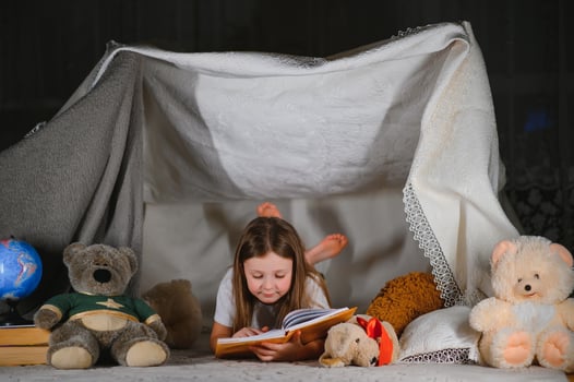 happy child girl laughing and reading book in dark in a tent at home. photo