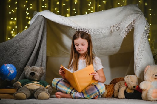 happy child girl laughing and reading book in dark in a tent at home. photo