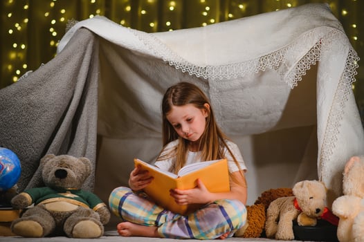 child girl reading with book and flashlight and teddy bear in tent. before going to bed. photo