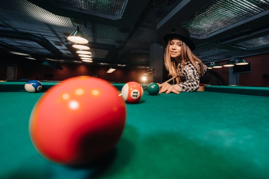 A girl in a hat in a billiard club with a cue in her hands hits a ball.Playing pool photo
