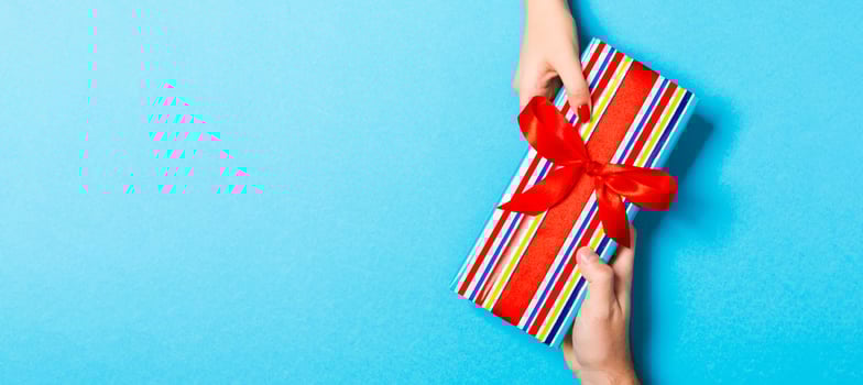 Top view of holding a gift in female and male hands on colorful background. Woman and man give and receive a present. Time for holiday concept with copy space photo