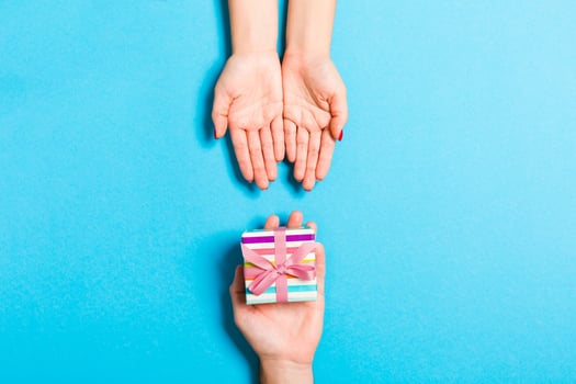 Top view of giving and receiving a present on colorful background. A man and a woman holding gift in hands. Close up of festive concept photo