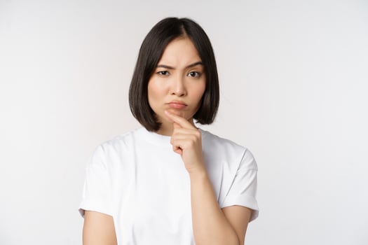 Thoughtful asian woman looking aside, pondering, making assumption, thinking or choosing smth, standing over white background photo