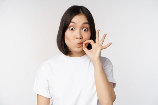 Image of young asian woman showing silence gesture, zipping mouth, seal lips, make promise, standing over white background photo