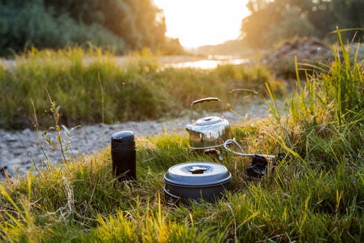 A close shot of a kettle and a thermos by the river bank in the grass. Dinner in nature, meal of a tourist. Hike to nature to the river. Kettle, thermos. photo