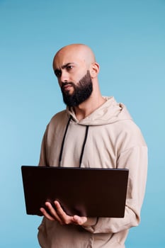 Puzzled arab man programming on laptop and looking away with confused expression. Confused person in doubt while developing software app and writing code on portable computer photo