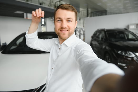 Young man is choosing a new vehicle in car dealership and making photo on a smartphone.