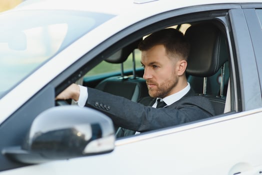 Always in a hurry. Handsome young man in full suit smiling while driving a car. photo