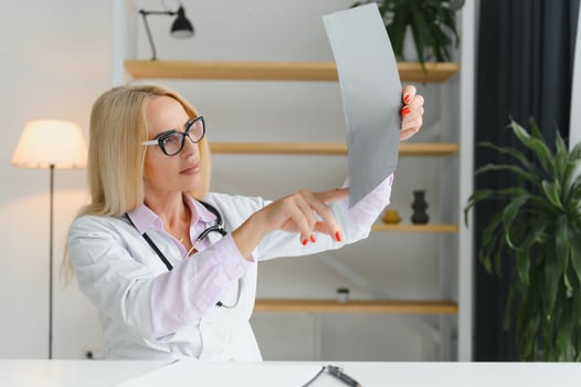 Portrait of middle age female doctor is wearing a white doctor's coat with a stethoscope around her neck. Smiling physician standing at private clinic photo