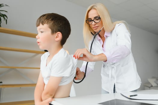 Pediatrician listening to breathing in the lungs and heartbeat with stethoscope. Portrait of adorable little boy visiting doctor. photo