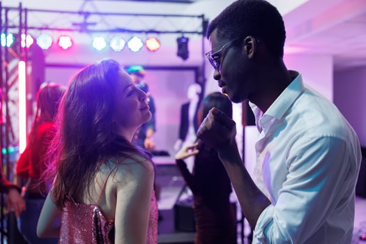 Couple in love dancing and clubbing while attending disco party in nightclub. Young diverse boyfriend and girfriend celebrating, moving to music rhythm on dancefloor illuminated with stage spotlights photo