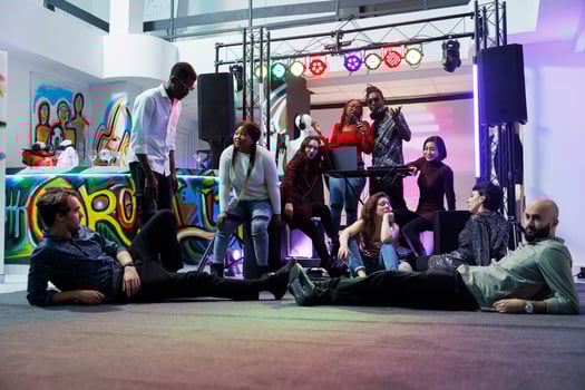 Music band performing on stage while diverse tired people lying and sitting on dancefloor. Exhausted young clubbers relaxing and listening to live music at club party gathering photo