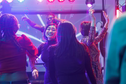 Happy diverse girlfriends partying and dancing at discotheque in nightclub. Cheerful smiling women moving to music beats, jumping and having fun on dancefloor in club with lights photo