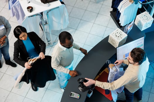 Cashier at clothing store checkout desk scanning and processing purchase for customer top view. Diverse people standing in line at counter desk while boutique employee using scanner photo
