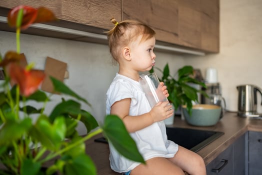 Happy baby girl sitting at the table in the kitchen and drinking milk photo