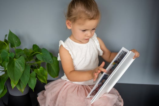 Happy cute little girl looking at photos in album. Happy smiling daughter browsing through printed family album, looking at pictures.