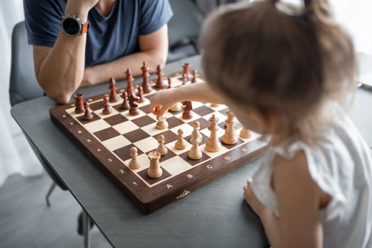 Little girl playing chess with her father at the table in home kitchen. The concept early childhood development and education. Family leisure, communication and recreation. photo